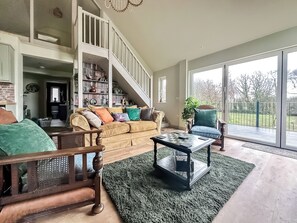 A spacious living room with a staircase, a large window, and a bookshelf.