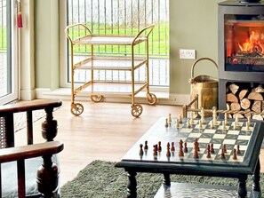 A living room with a chessboard, a wooden cart, a fireplace, and a window with a view of greenery.