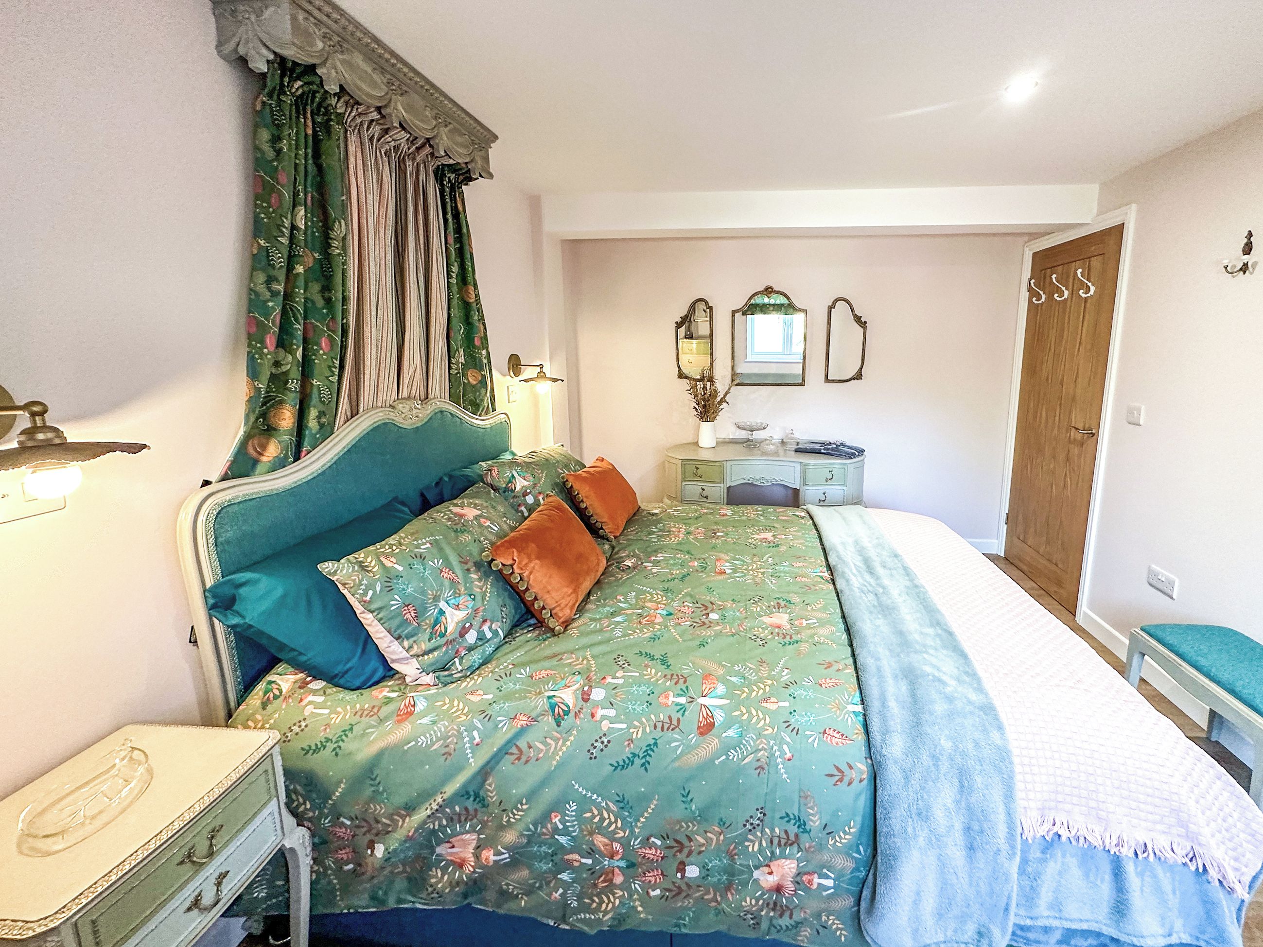 Une chambre à coucher comprenant un lit, une table de chevet, une commode, un miroir et une porte.