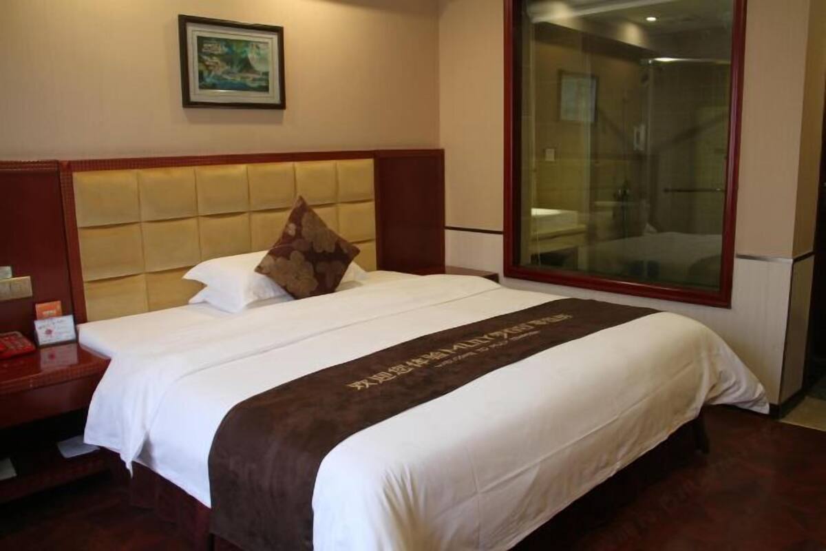 Una habitación de hotel con una cama, una mesita de noche, un cuadro enmarcado en la pared y un ventanal grande.