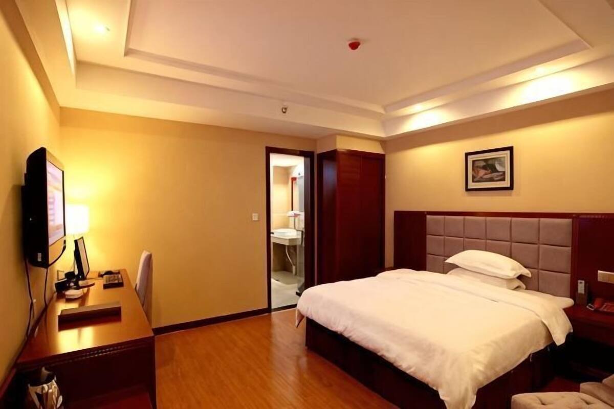 Habitación de hotel con cama, escritorio con lámpara, televisión y puerta que da a un baño.