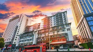 A multi-story building with commercial spaces on the ground floor, a red bus in front, and a sunset sky. - Fulante Le Hotel (Tianmen Mountain Fengwan Road) (Zhangjiajie)