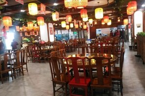 Um restaurante com várias mesas redondas e cadeiras, luminárias pendentes no teto e piso ladrilhado.