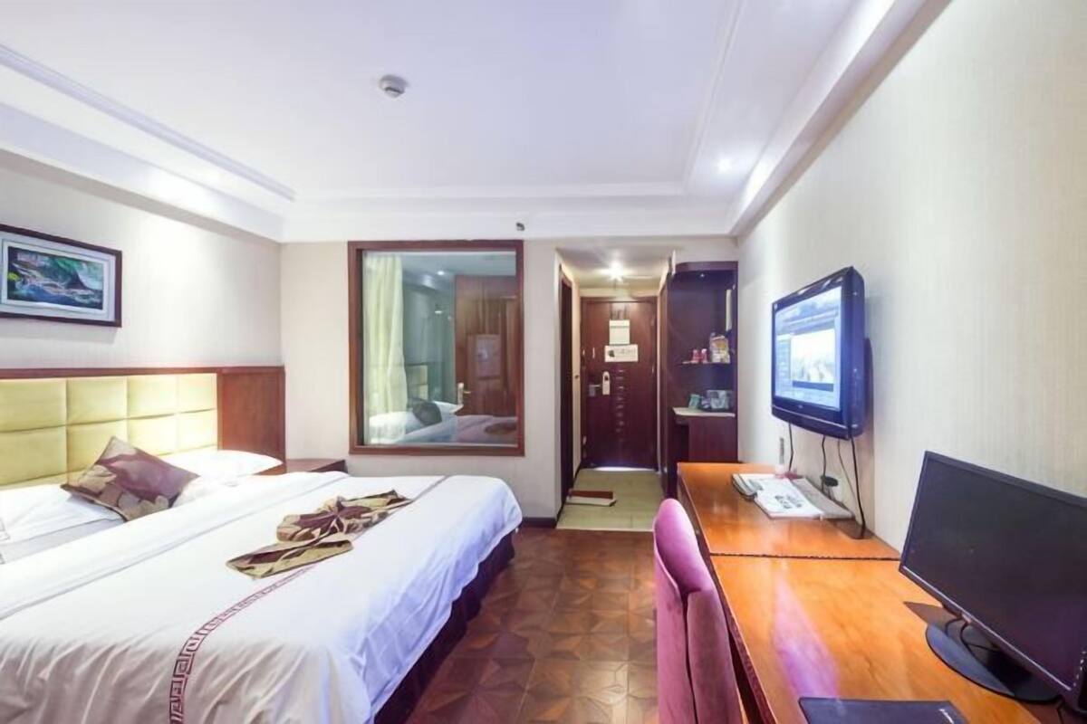Una habitación de hotel con una cama, un escritorio con computadora, un televisor y un espejo.