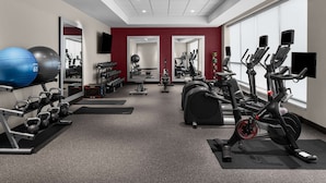 Un gimnasio con equipo de ejercicio, espejos y una pared de acento roja.