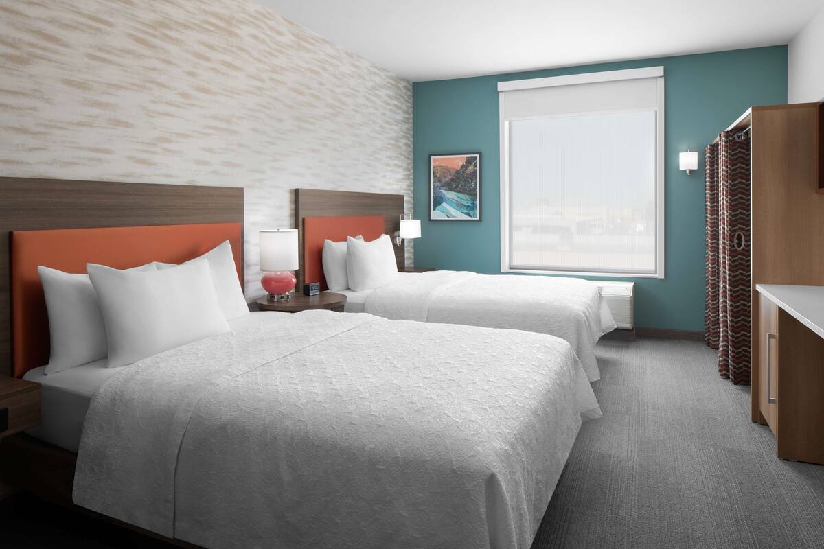 A hotel room with two beds, a large window, a painting, and a view of the city.