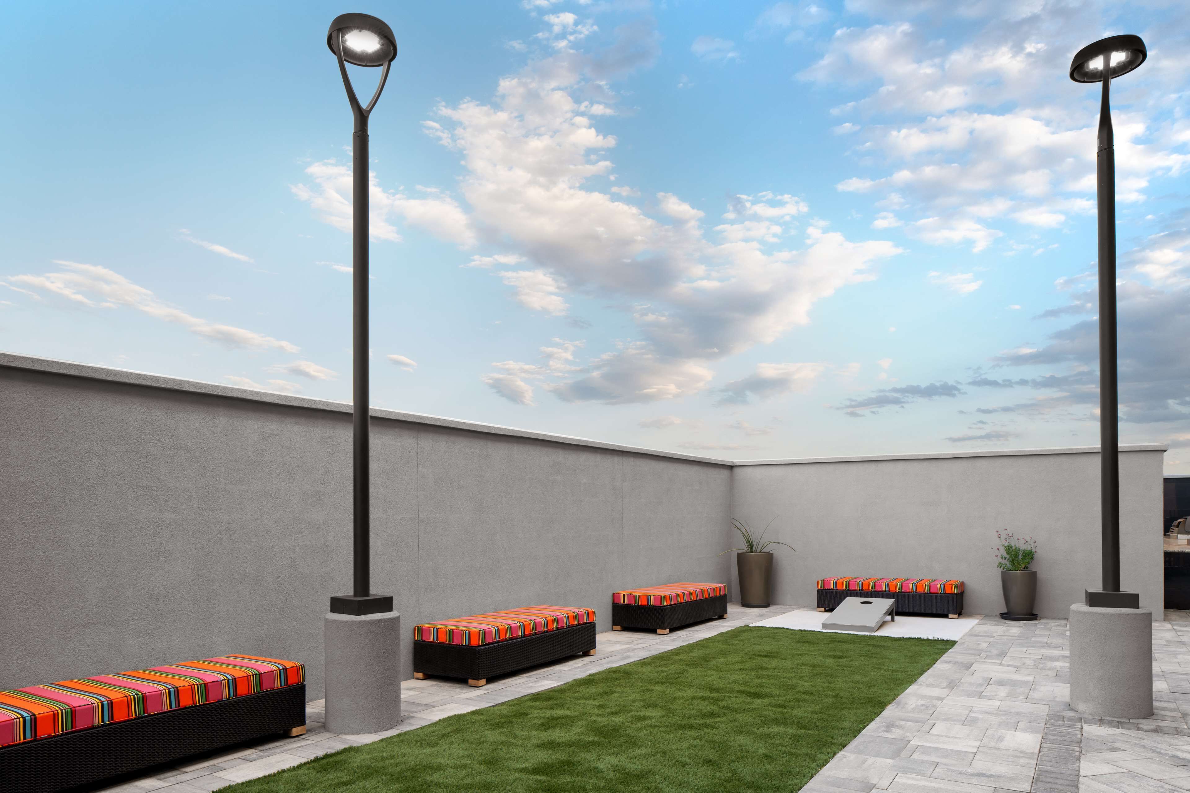 An outdoor seating area with benches and a small lawn, surrounded by walls and a sky with clouds.