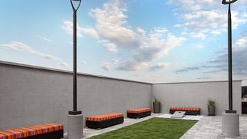 An outdoor seating area with benches and a small lawn, surrounded by walls and a sky with clouds.