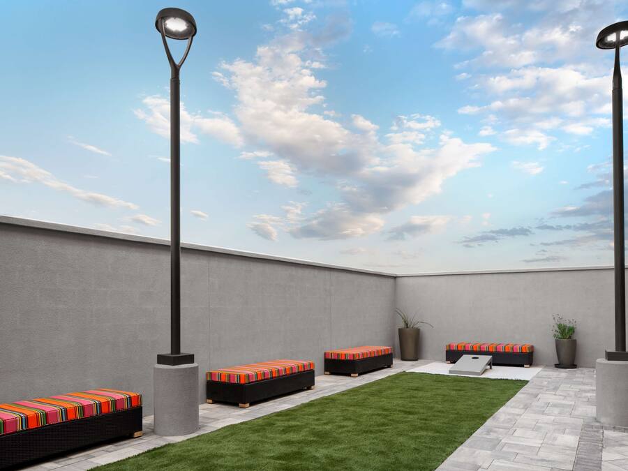 An outdoor seating area with benches and a small lawn, surrounded by walls and a sky with clouds.