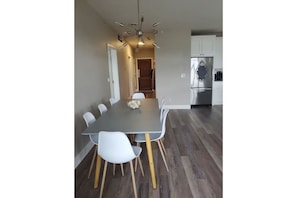 A modern kitchen with a stainless steel refrigerator, a dining area with a grey table and white chairs, and a wooden floor. - 3 Bdrm Wine Country Luxury Waterfront Condo (West Kelowna)