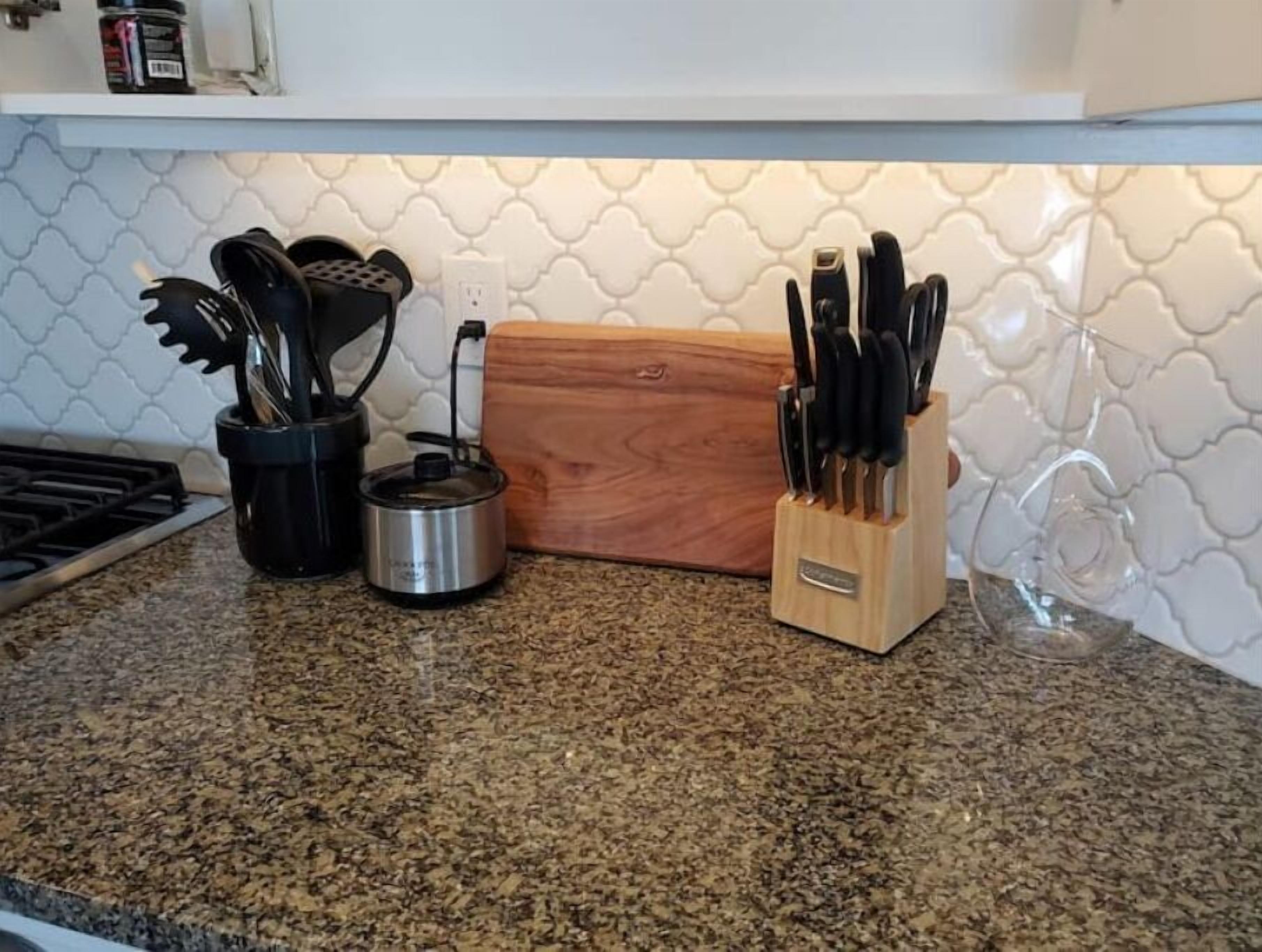 Una encimera de cocina con estufa, tetera, tabla de cortar de madera y bloque para cuchillos.