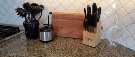 Una encimera de cocina con estufa, tetera, tabla de cortar de madera y bloque para cuchillos.