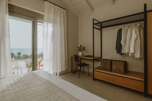 Un dormitorio con cama, un escritorio con silla, un perchero y vista al mar.