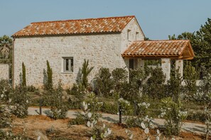 A stone building with a tiled roof, surrounded by a garden with various plants and a dirt path. - Nama Seaside Villas (Preveza)