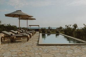 A poolside area with lounge chairs and umbrellas, a stone-tiled floor, and a view of the sea. - Nama Seaside Villas (Preveza)