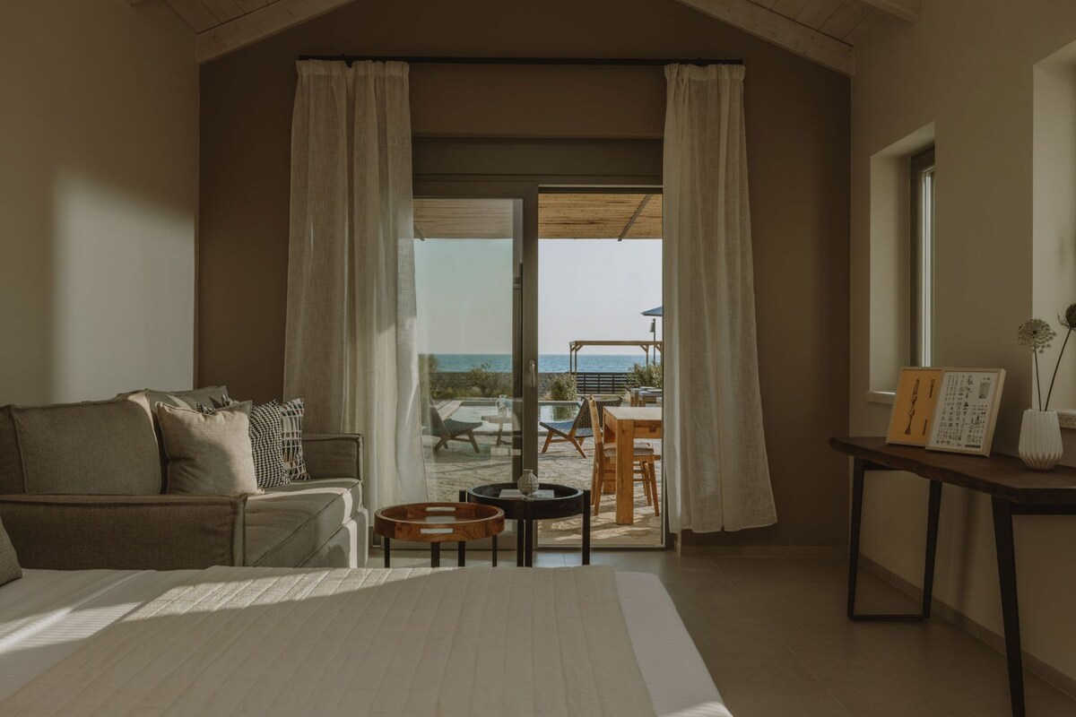 Un dormitorio con una cama grande, un sofá, una mesita y vistas a un patio exterior con mesa y sillas.