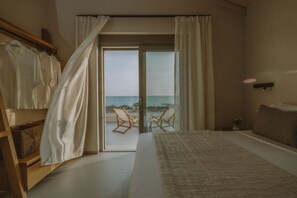 A bedroom with a large bed, a view of the sea through a sliding glass door, and a balcony with chairs. - Nama Seaside Villas (Preveza)