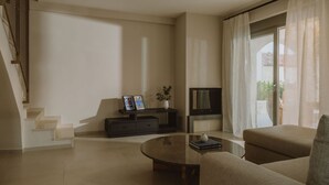 A modern living room with a sofa, a coffee table, a TV, and a staircase. - Nama Seaside Villas (Preveza)