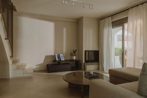 A modern living room with a sofa, a coffee table, a TV, and a staircase. - Nama Seaside Villas (Preveza)