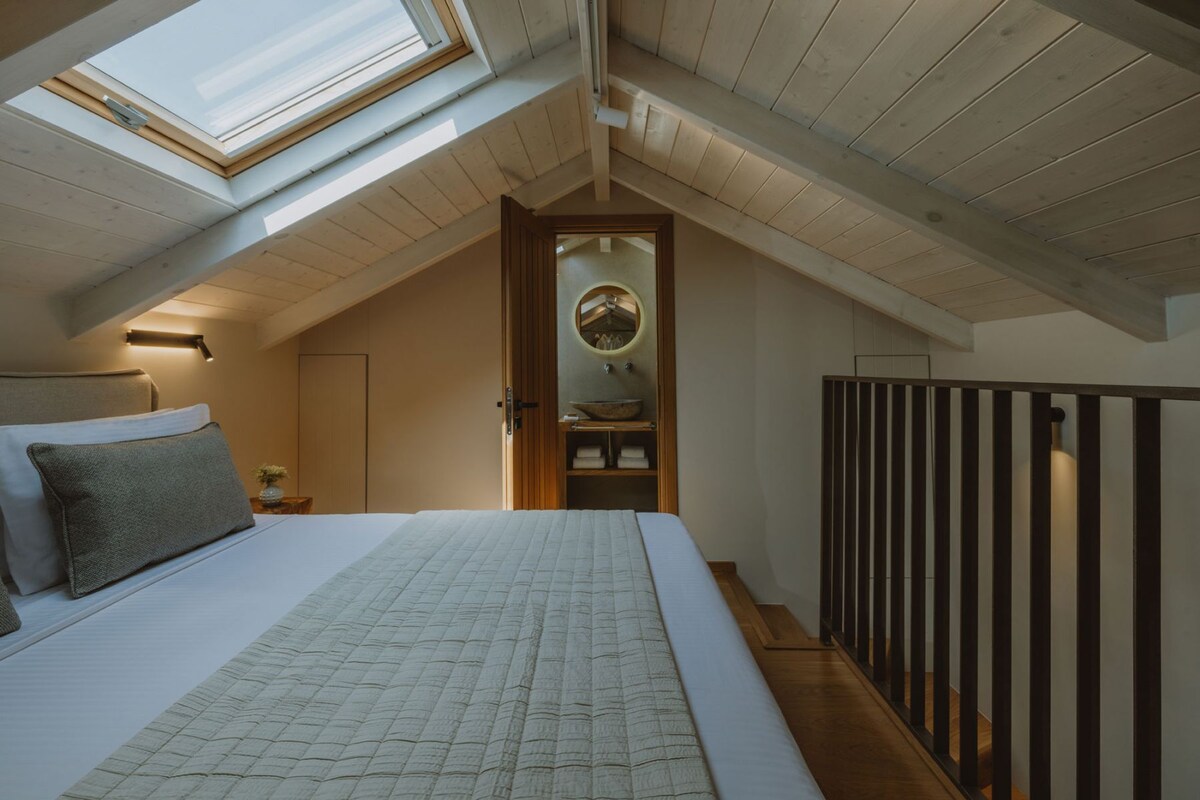 Une chambre avec un puits de lumière, un lit, une table de chevet, un miroir et une rambarde en bois.