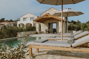 Un área junto a la piscina con sillones de descanso, una mesa y sombrillas.
