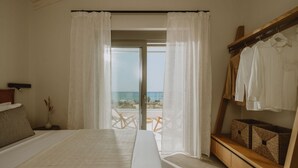 A bedroom with a large bed, a wooden bench with storage, a view of the beach, and a balcony with a table and chairs. - Nama Seaside Villas (Preveza)