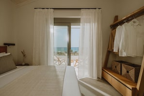 Une chambre avec un grand lit, un banc en bois doté de rangements, une vue sur la plage et un balcon avec une table et des chaises.