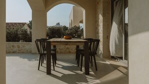 An outdoor patio with a table and chairs, surrounded by stone walls and arches, overlooking a residential area. - Nama Seaside Villas (Preveza)
