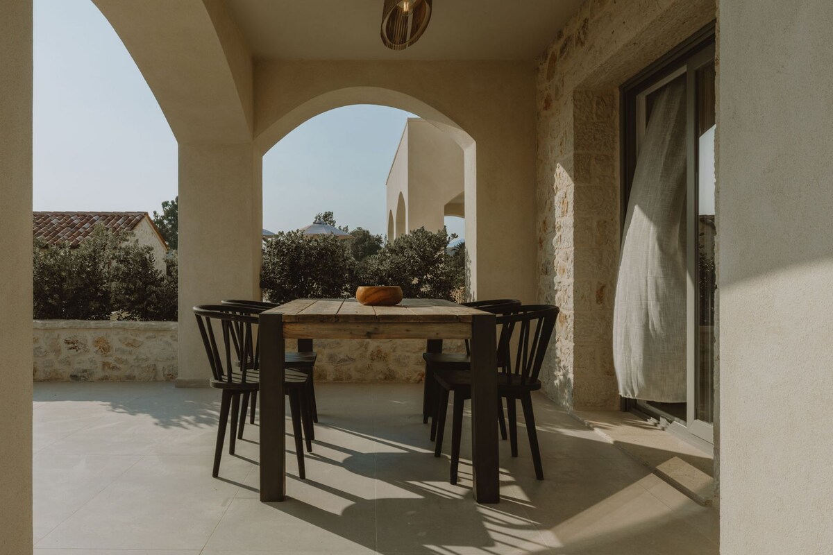 An outdoor patio with a table and chairs, surrounded by stone walls and arches, overlooking a residential area.