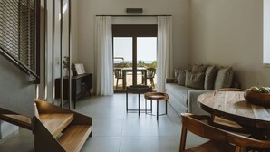 A spacious living area with a large window, a wooden table, and a sofa. - Nama Seaside Villas (Preveza)