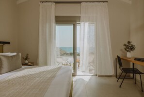 Un dormitorio con cama, escritorio, silla y vistas al mar desde un balcón.