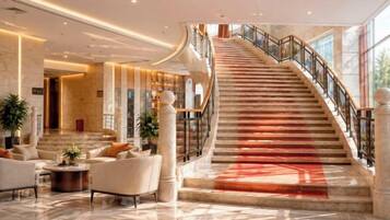 A grand lobby with a marble floor, a curved staircase, and a seating area with sofas and a coffee table.