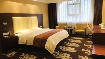 A hotel room with a bed, a desk, two chairs, a small table, and a window with curtains.