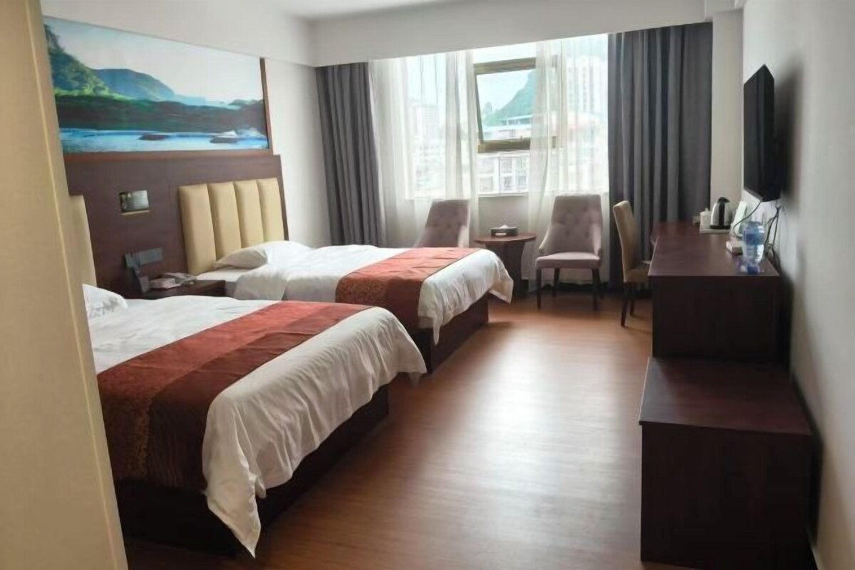 A hotel room with two beds, a desk, a chair, a TV, and a window with curtains.