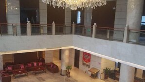 A spacious lobby with a high ceiling, marble flooring, and a chandelier. There are seating areas with sofas and a potted plant. - Ningxin International Hotel (Luocheng)