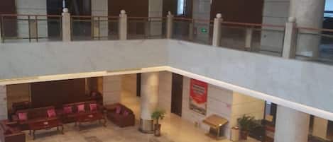 A spacious lobby with a high ceiling, marble flooring, and a chandelier. There are seating areas with sofas and a potted plant.