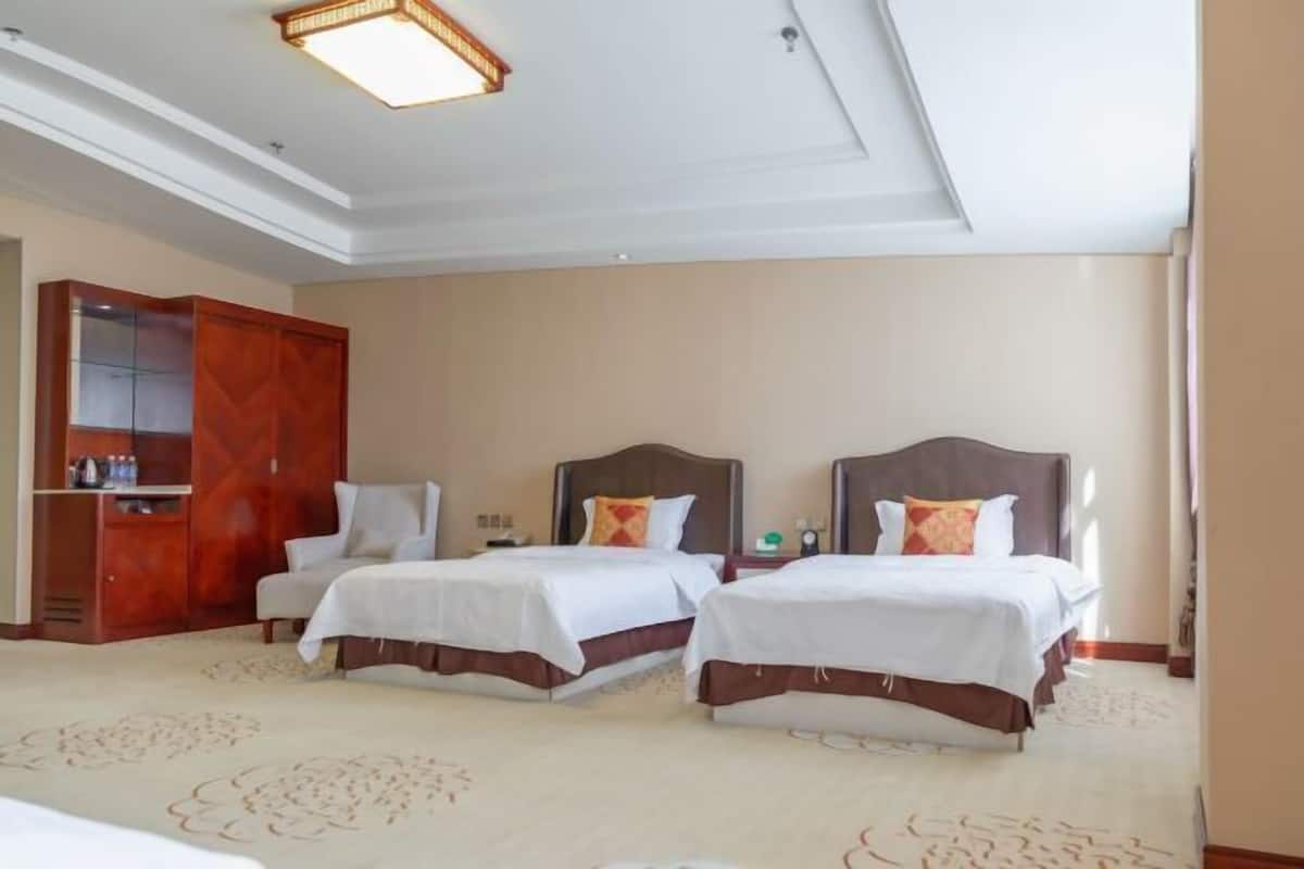 Habitación de hotel con dos camas, un armario de madera, una lámpara en el techo y suelo alfombrado.