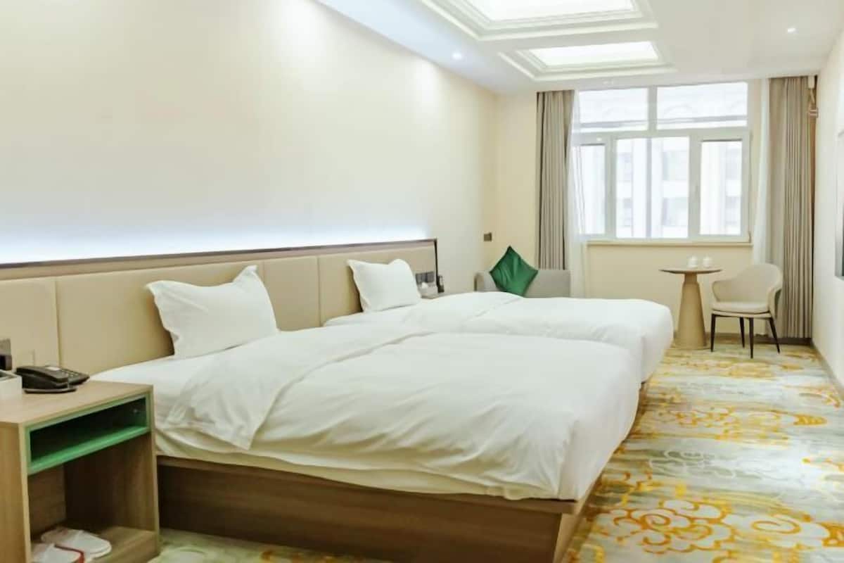 Habitación de hotel con dos camas, una mesita, una silla y un ventanal con cortinas.