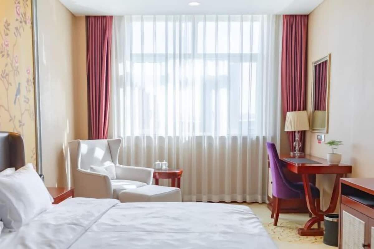 Habitación de hotel con cama, escritorio, silla y un amplio ventanal con cortinas.