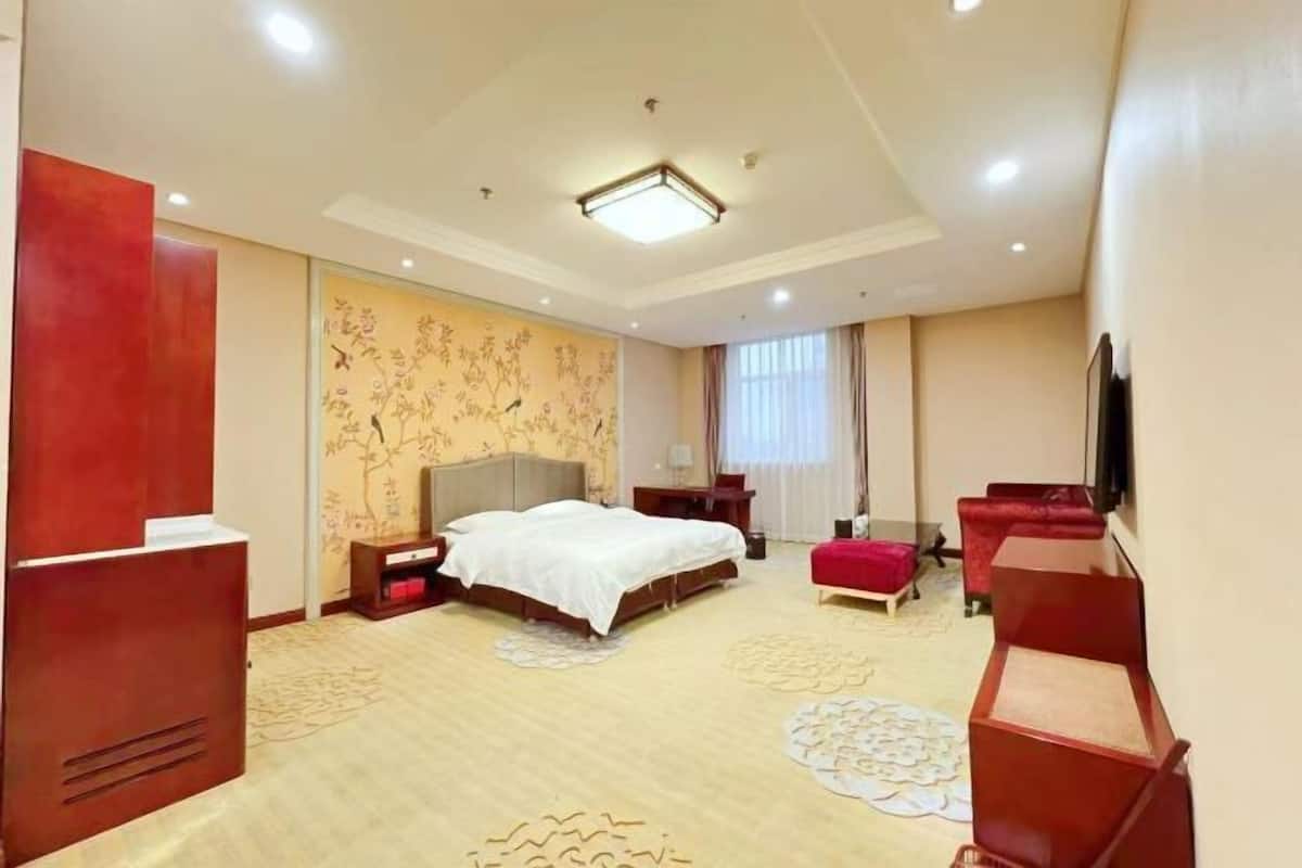 Habitación de hotel con cama, escritorio, silla, televisión y un ventanal grande.