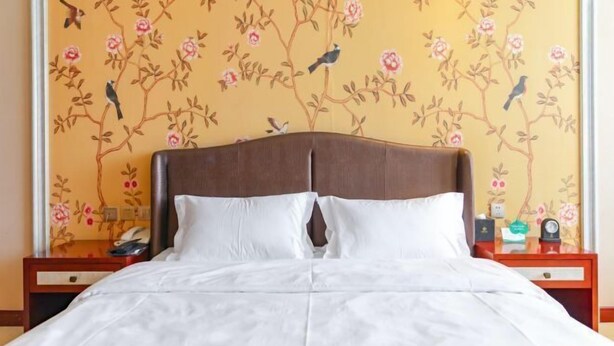 Una cama con sábanas blancas en una habitación con papel tapiz floral y cabecera de madera.