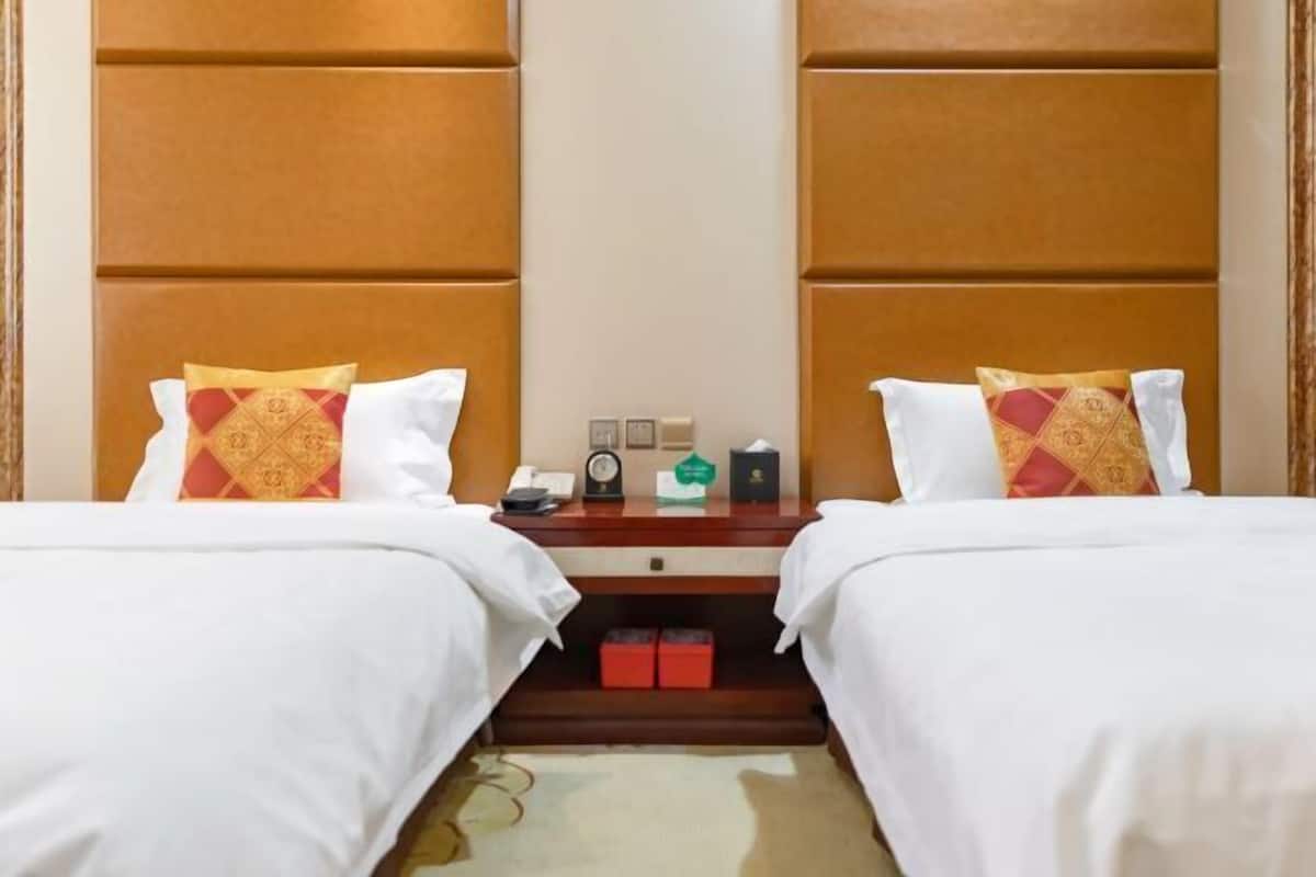 Habitación de hotel con dos camas, una mesita de noche, un reloj, un teléfono y una pequeña mesa con un objeto verde.