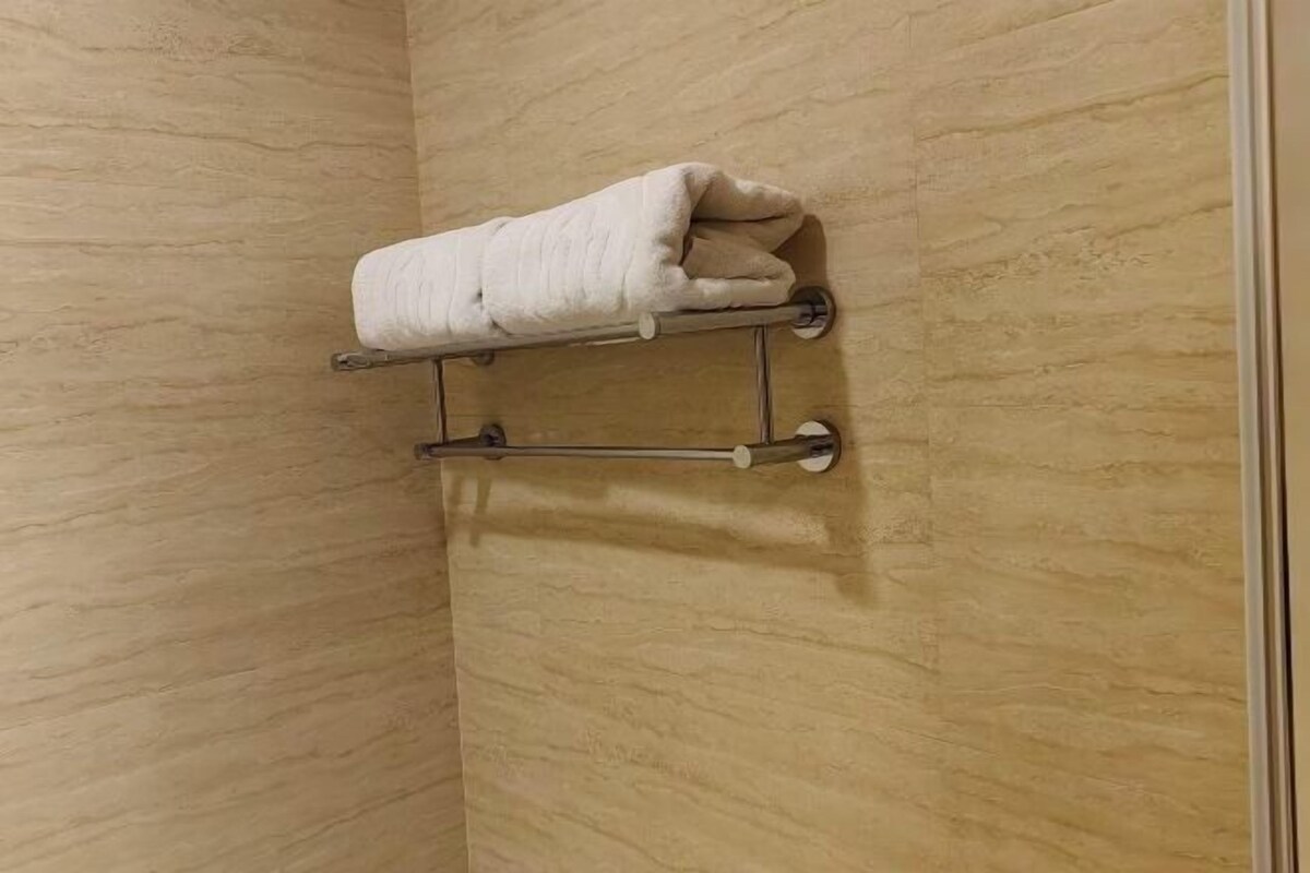 A bathroom with a beige textured wall, a towel rack with a folded towel, and a metal towel bar.