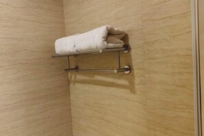 A bathroom with a beige textured wall, a towel rack with a folded towel, and a metal towel bar.