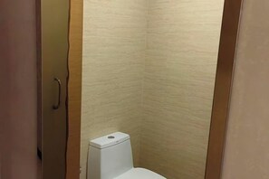 A small, enclosed bathroom with a toilet, a door, and a textured wall.