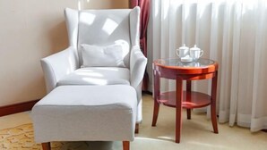 Una habitación con un sillón gris, una mesita redonda de cristal y una ventana con cortinas.