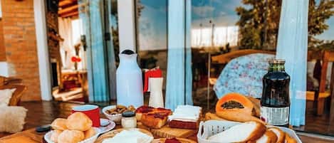A table set with various food items, including bread, cheese, and cured meats, with a bottle and cups on the table.