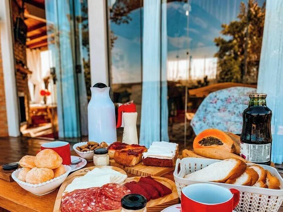 A table set with various food items, including bread, cheese, and cured meats, with a bottle and cups on the table.
