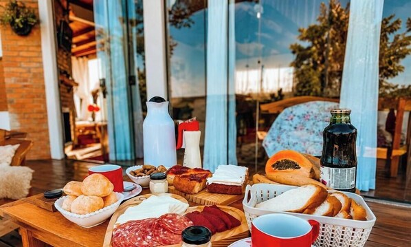 Ein Tisch reichhaltig mit Speisen gedeckt, darunter Brot, Käse und Wurstwaren, mit einer Flasche und Tassen darauf.