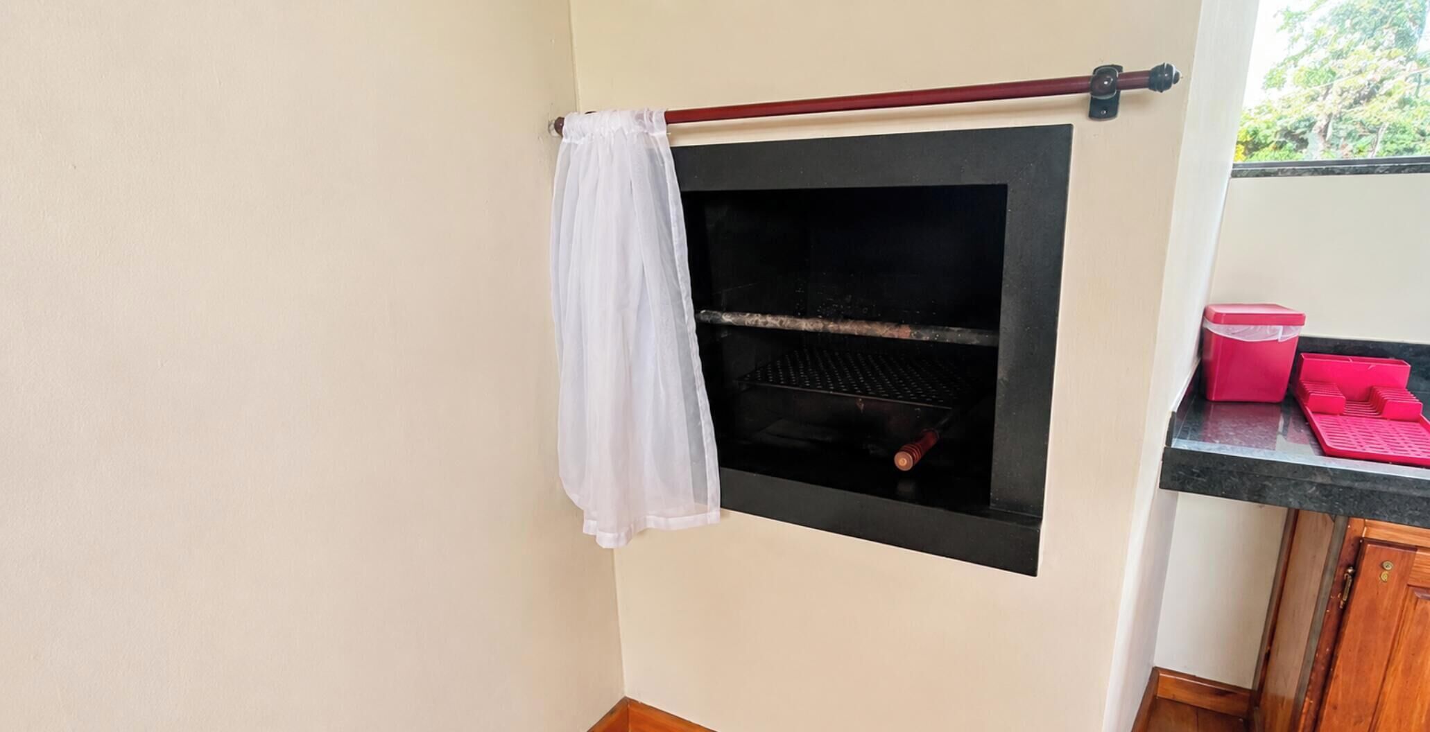 Un piccolo spazio chiuso con una griglia, un panno bianco e un contenitore rosso su un bancone.